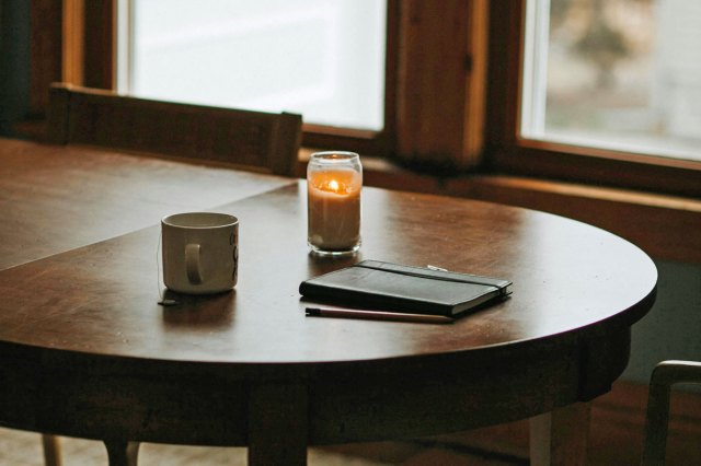 A candle, journal and candle sitting on a wooden table 