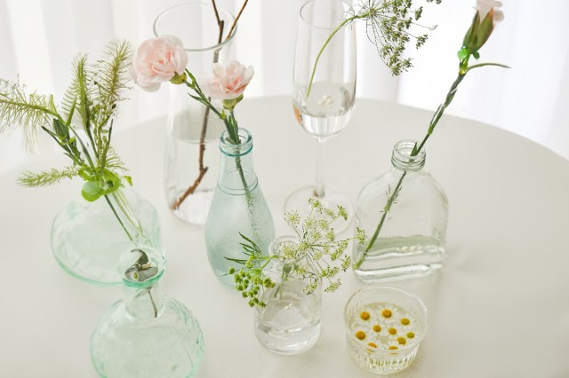 A white table topped with clear glasses with flowers in them