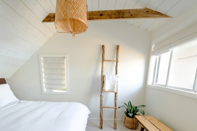 A white bedroom with a hanging light and a wooden beam on the ceiling