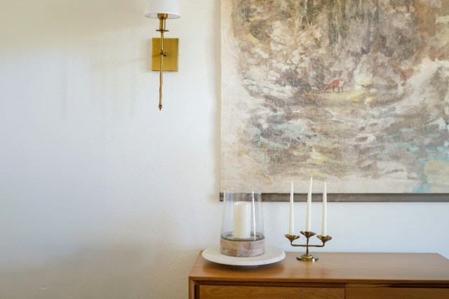 A painting hanging over a wooden dresser next to a sconce
