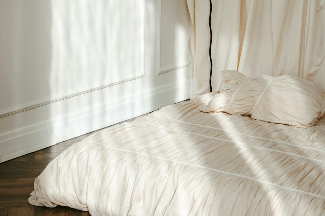 A mattress made on the floor next to a floor lamp 