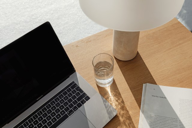 A laptop sitting on a wooden desk with a cup of water